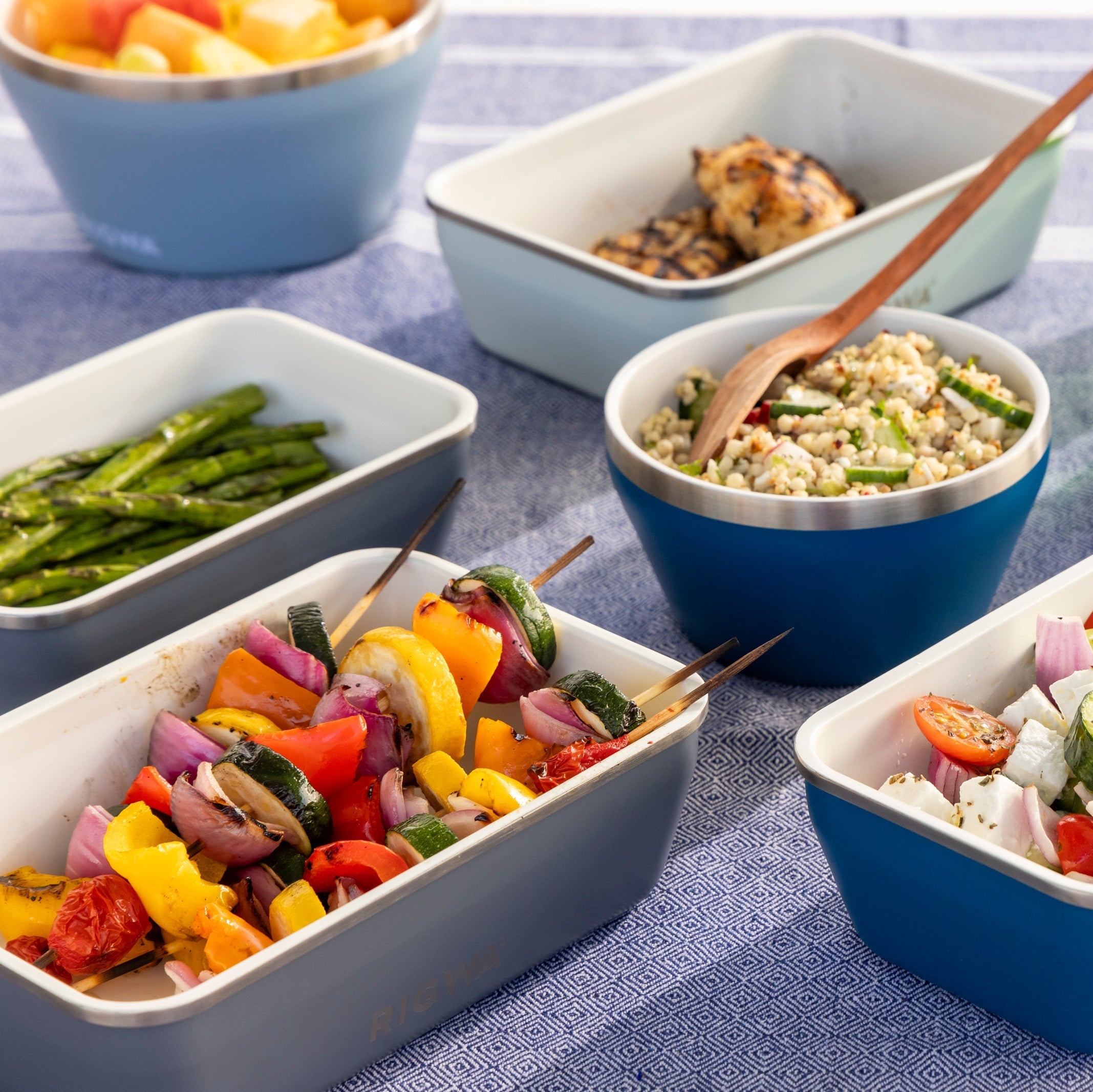 Assorted dishes of food including vegetables and grains on a blue tablecloth.
