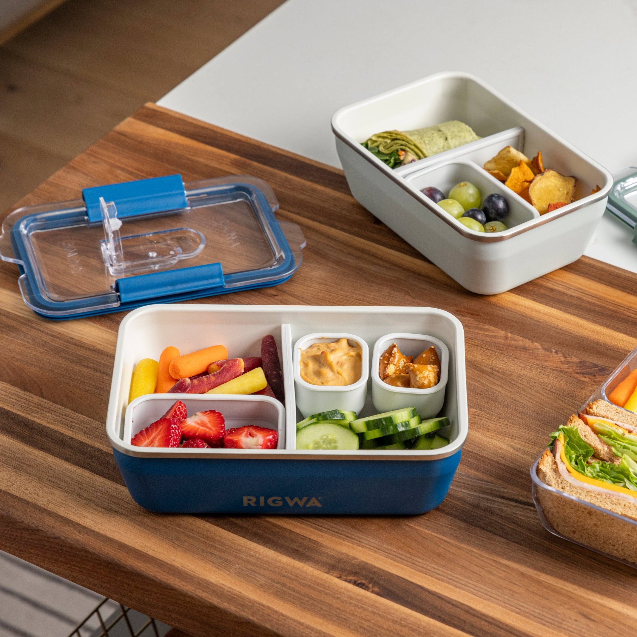 Bento boxes with compartments containing various food items on a wooden table.