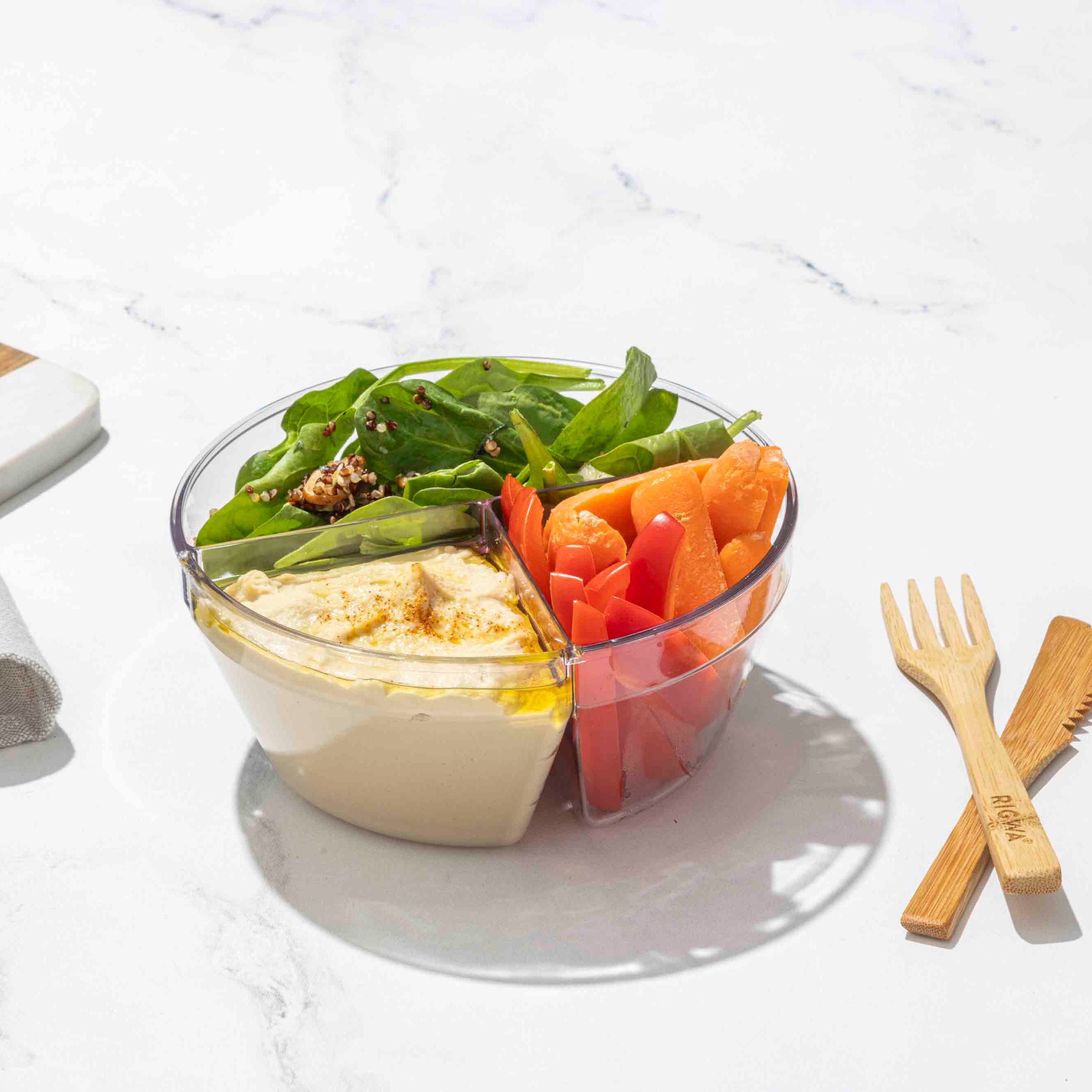 Bowl of salad with vegetables and a wooden fork and knife on a white surface