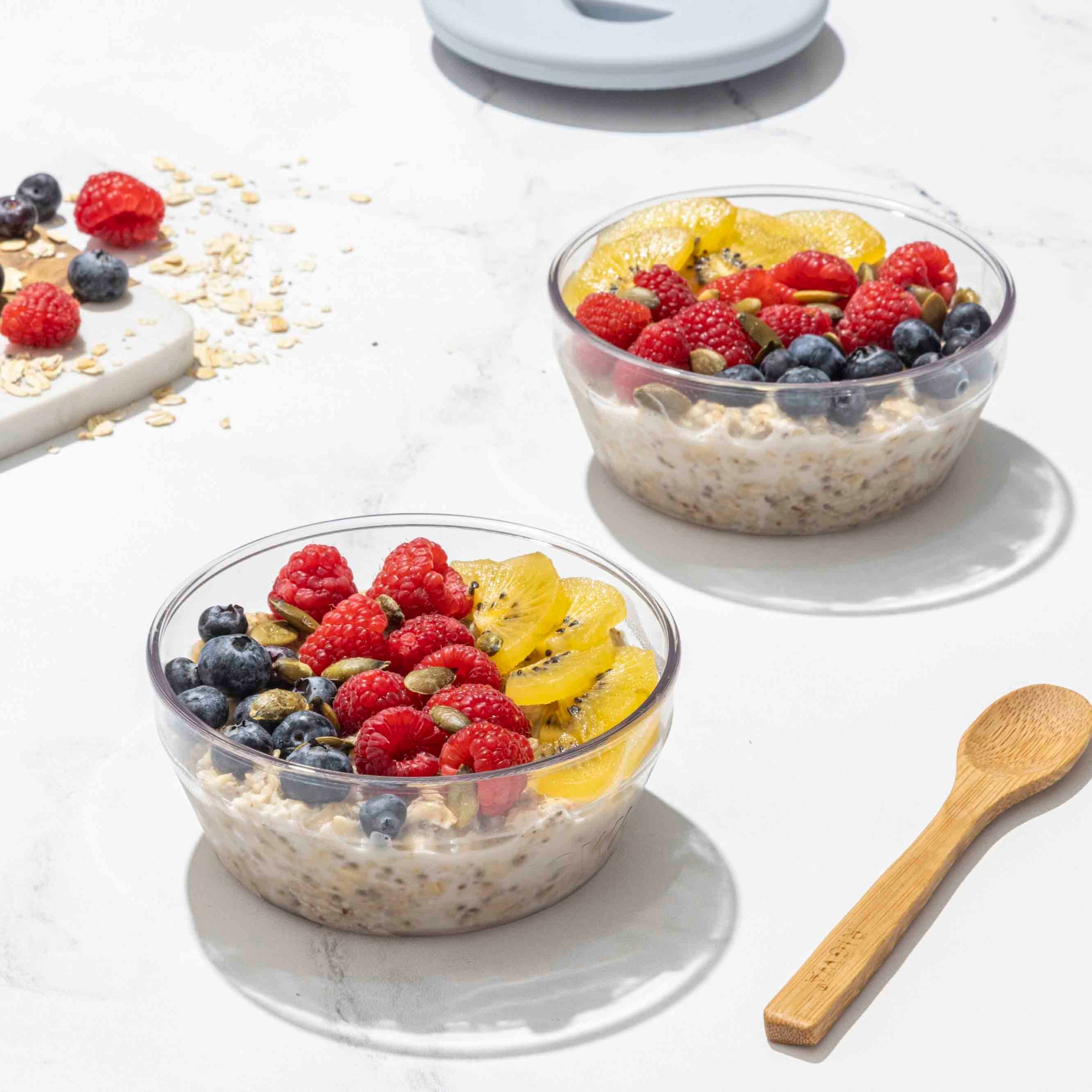 Two bowls of oatmeal with fruit on a white surface