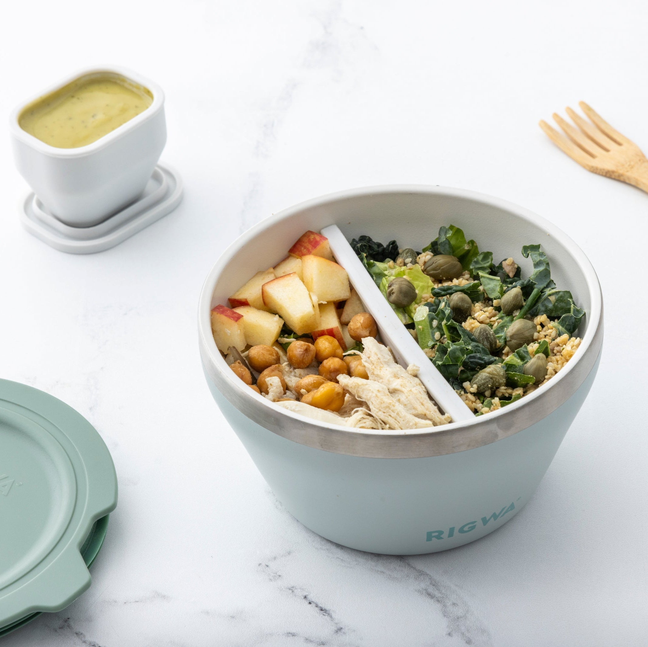 Meal prep bowl with salad and side dish on a marble surface, featuring a fork and small container.